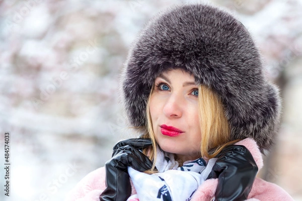 Fototapeta happy woman in a pink faux fur coat in winter on a background of snowy trees