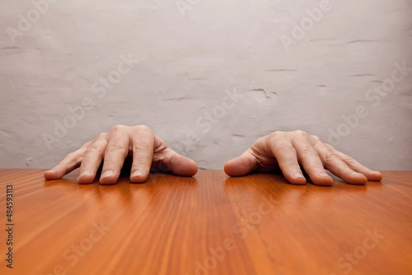 Fototapeta Men's hands resting on the top of a wooden table.