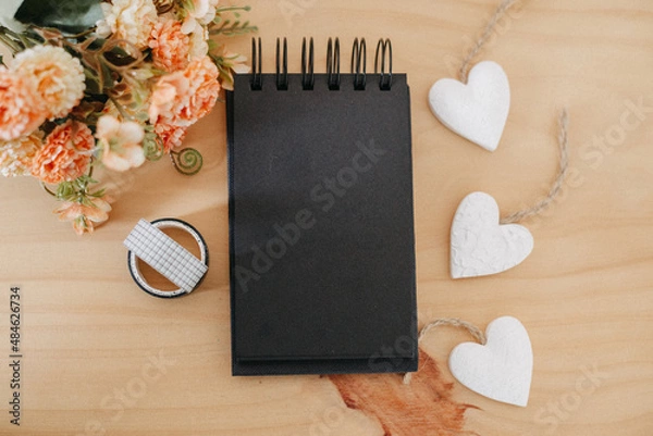 Fototapeta notebook with black sheets with copy space, bouquet of flowers and a white heart.