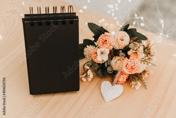 Fototapeta notebook with black sheets with copy space, a bouquet of flowers and a white heart