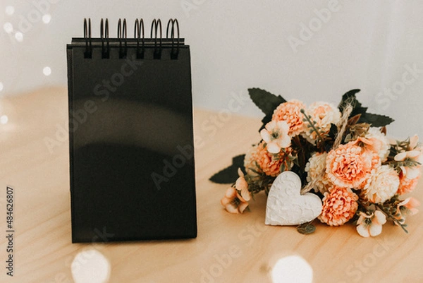 Fototapeta notebook with black sheets with copy space, a bouquet of flowers and a white heart