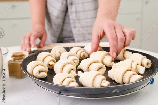 Fototapeta raw mini croissants with cinnamon on a baking tray in a bright home kitchen. Female farts in the frame