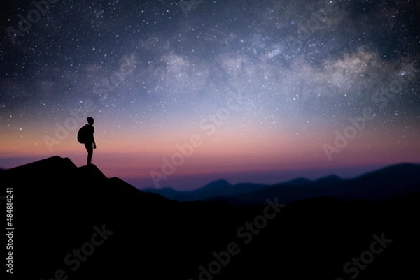 Fototapeta Silhouette of young male traveler with backpack standing and watching the star, milky way over the sky alone on top of the mountain. He enjoyed traveling and was successful when he reached the summit.