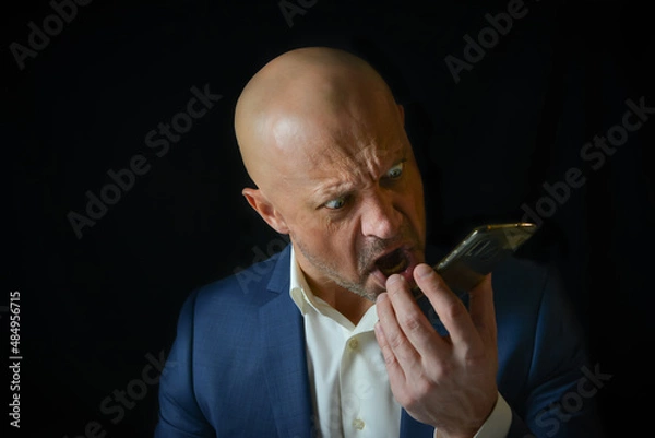 Obraz A man in a business suit emotionally swears on the phone. Enraged and angry boss screams into the telephone receiver.