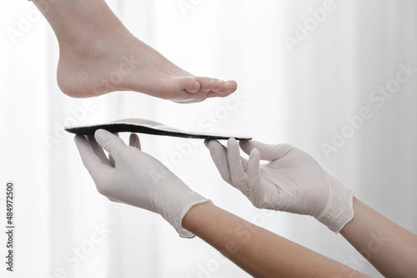 Fototapeta Orthopedic insole on a white background. Hands in rubber gloves hold an orthopedic insole. Foot care, comfort for the feet. Doctor orthopedist tests the medical device. Flat feet correction.