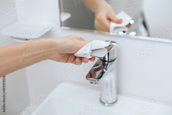 Fototapeta Cleaning the sink faucet with a microfiber cloth. Cleaning the bathroom. Sanitize surfaces prevention in hospital and public spaces against corona virus. Woman hand using wet wipe