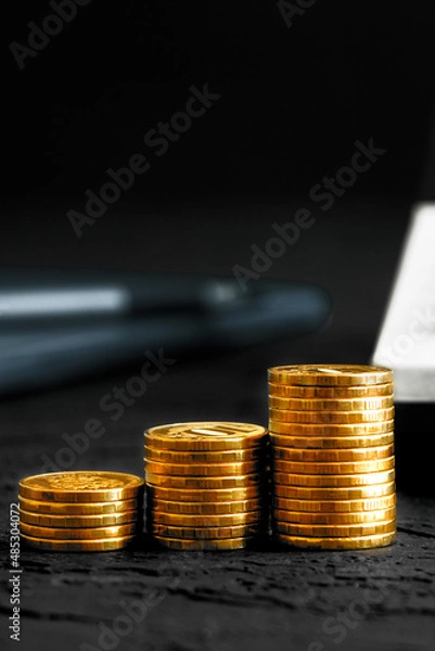 Fototapeta A stack of gold coins isolated on a black background.Money on a black background.Finance and money.Vertical orientation