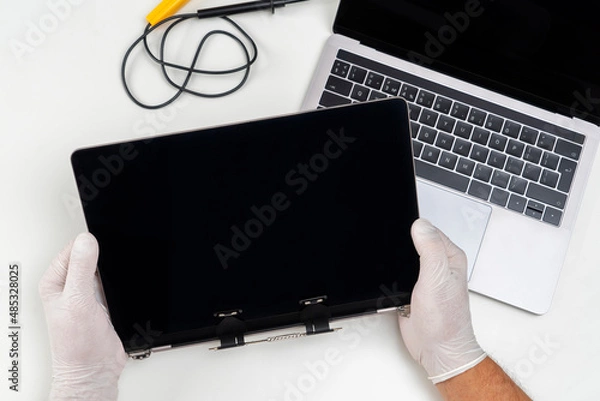 Fototapeta A man replaced a broken monitor on a laptop and holds it in his hands in a light white room.