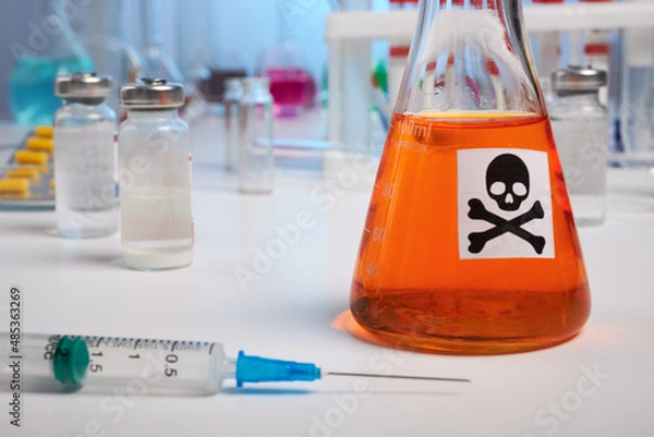 Fototapeta Orange toxin flask and syringe - lab photo. Orange poisonous liquid inside chemical retort. Syringe for death injection on a desk surface. Colored liquids inside chemical flasks, retorts, test-tubes.