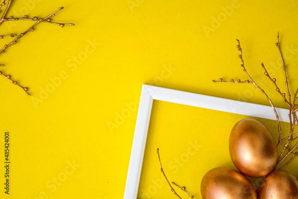 Fototapeta Golden Easter eggs and golden branches on a yellow watercolor background. Banner. Layflat. Space for text 