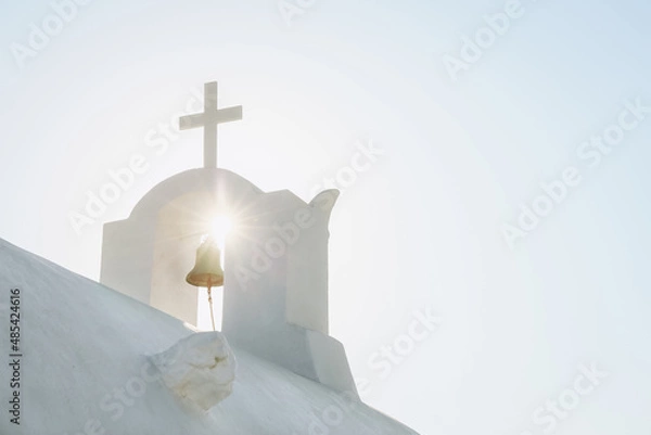 Fototapeta White Orthodox Church belfry with cross and bell in sunshine on sky background. Santorini island, Greece
