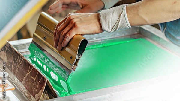 Fototapeta silk screen textile printery. male hand with a squeegee. creating print on t-shirt in workshop. serigraph printing production