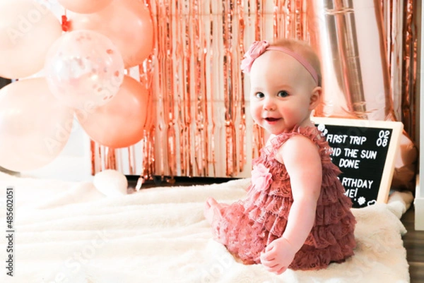 Obraz Cute birthday girl celebrating her one year birthday by messily eating a cake surrounded by pink background streamers and balloons