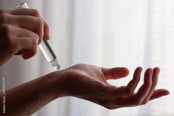 Fototapeta Closeup of a woman using rollerball perfume on her wrist.