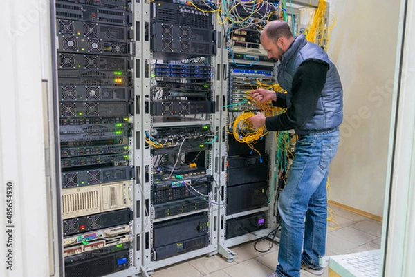 Obraz A technician works in a server room. Support for the network information infrastructure of the data center. Man connecting server with fiber optic cable