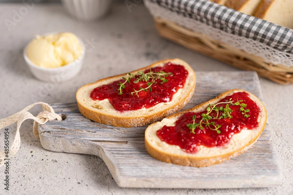 Fototapeta White bread slices with butter and raspberry jam on it, greens on wooden board, organic country sweet sandwich, homemade dessert. Copy space.