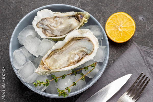 Fototapeta Oysters with ice in bowl. Lemon knife and fork on table.
