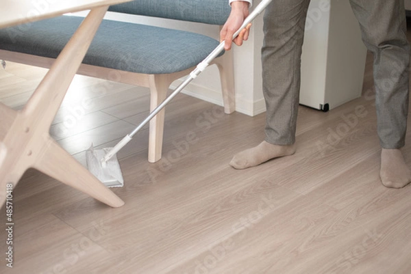 Obraz A Japenese young Asian man hoovers the floor using a vacuum cleaner in a house with a desk and two chairs