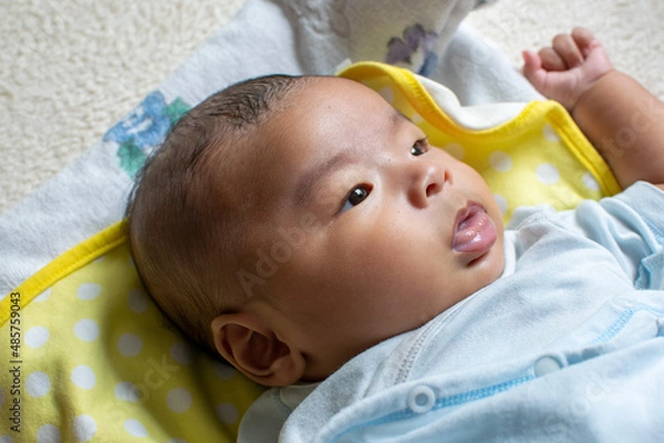 Obraz A Japanese Asian infant baby lying down on the white carpet looks at his mother with blue clothes