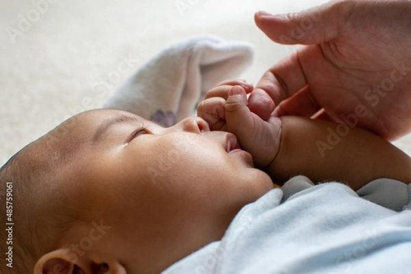 Obraz A Japanese Asian infant baby with blue clothes holds his mother's finger