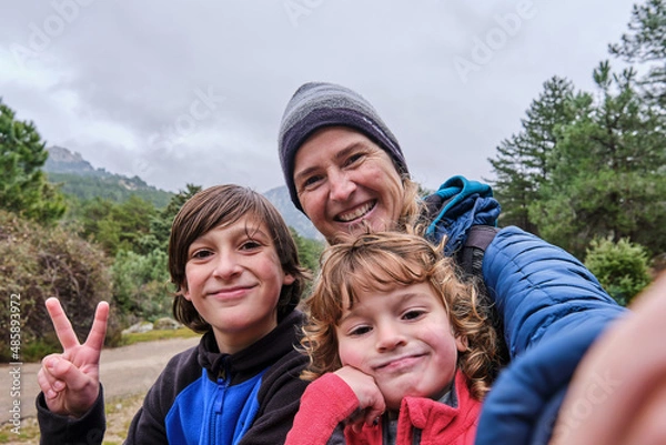Obraz A happy family taking a selfie portrait with smartphone in the mountains in winter