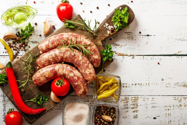 Fototapeta Bratwurst or sausages with spices and greens on a cutting board. On a white wooden table.