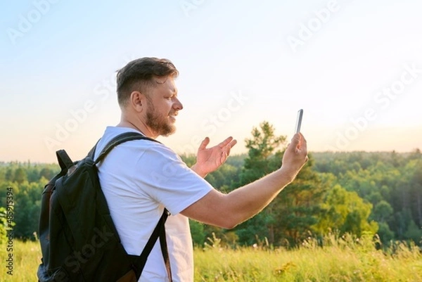 Fototapeta Middle aged bearded man with smartphone backpack on hike, making video call