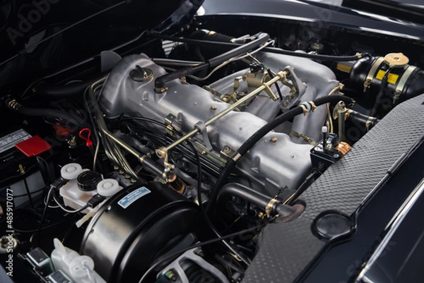 Fototapeta Look under the hood of a retro car in perfect condition, clean engine, lots of levers, hoses and wires, vintage