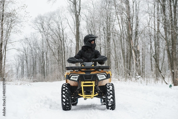 Fototapeta Man on a quad bike in winter background. Portrait of a quadricycle rider in snowy forest