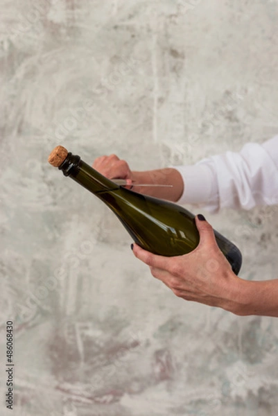 Fototapeta Sabre wine. A woman's hand opens a bottle of champagne with a knife. Gray background. Place for text