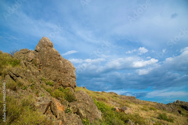 Fototapeta Summer hilly landscape. Rocks with green bushes.against the blue sky. The golden hour. The concept of nature