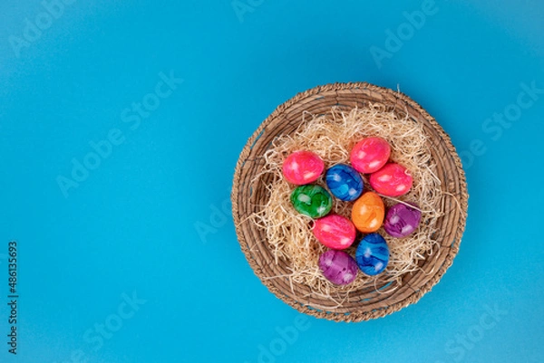 Fototapeta Easter eggs in a basket on a blue background, top view, copy space.