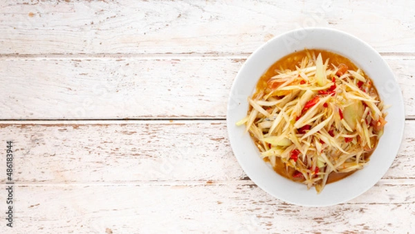 Obraz Som Tum Pla Ra, Thai E-San food, spicy papaya salad with pickled fish, tomato, lime and chilli in white ceramic plate on white wood texture background with copy space for text, top view