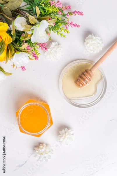 Fototapeta A jar of flower honey, honey on a saucer with a spoon and flowers on a white background. Flatlay. Top wiew