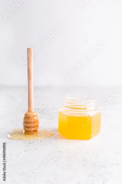 Fototapeta A jar of flower honey with a spoon on a light background. Minimalism