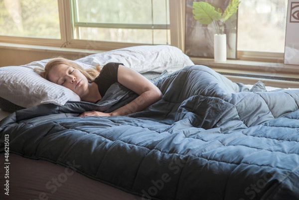 Fototapeta Young redhead woman using soft weighted blanket in her modern apartment while sleeping
