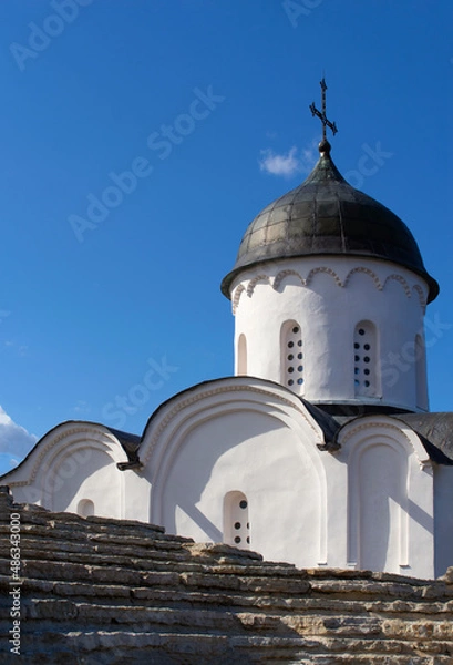 Fototapeta Close-up of the view from the stone wall to the upper part of the Orthodox church. White stone single-domed church. Blue sky with clouds. Daylight.