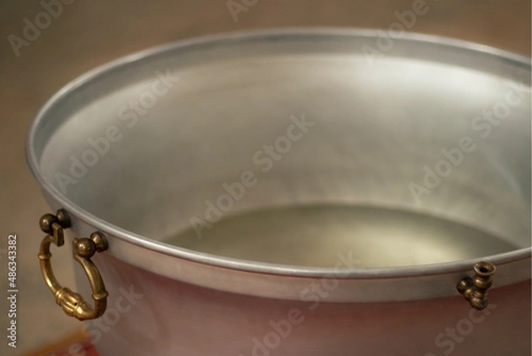 Fototapeta The edge of the baptismal bath. The handle and the tap are visible. Clear water is poured. Blurred background and foreground.