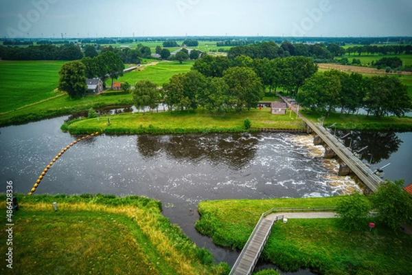 Fototapeta Drone view of the river Vecht, green grass, trees, beautiful blue sky and cycle path through the Vecht valley. Bridge and weir in the river. Dalfsen Netherlands