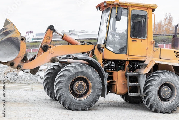 Fototapeta The loader is transporting sand or gravel in the front bucket. Heavy construction equipment at a construction site. Transportation of bulk materials in a concrete plant.
