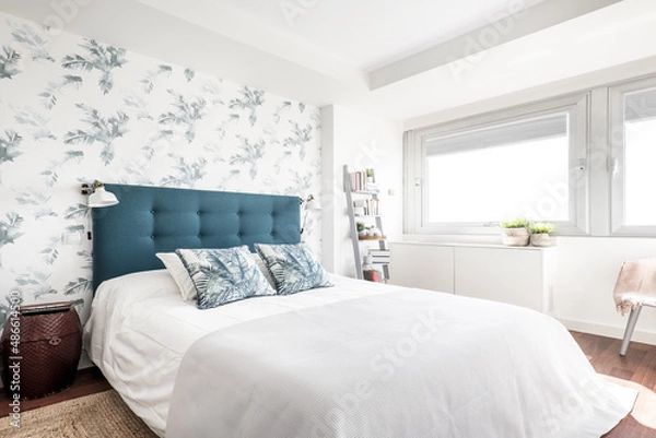 Fototapeta bedroom with a king size bed with a blue upholstered headboard and wallpapered walls with plants matching the cushions
