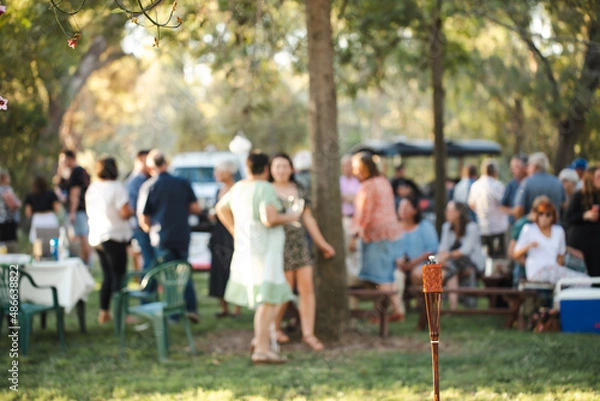 Fototapeta Unlit tiki torch or citronella lantern at garden party with guests out of focus in background