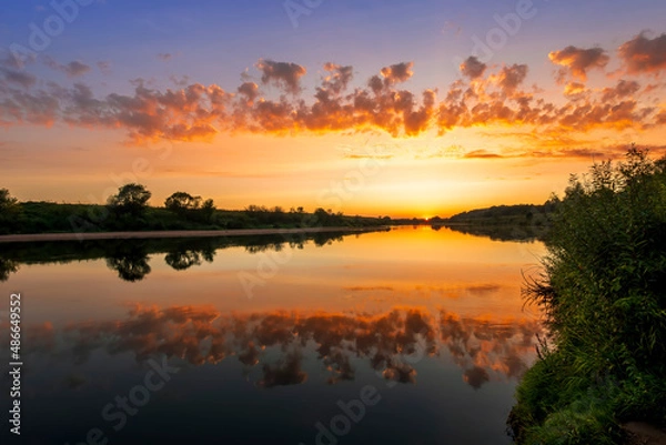 Fototapeta Amazing view at scenic landscape on a beautiful river and colorful sunset with reflection on water surface and glow on a background, spring season landscape