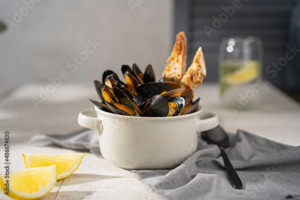 Fototapeta Cooked, boiled mussels with lemon juice, parsley and toasted bread in white bowl (plate) on the table. Seafood, copy space. 