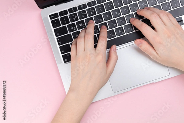 Fototapeta Female hands and laptop keyboard on a pink background. Concept workspace, work at the computer, freelance and design. Flat lay, top view and copy space photo