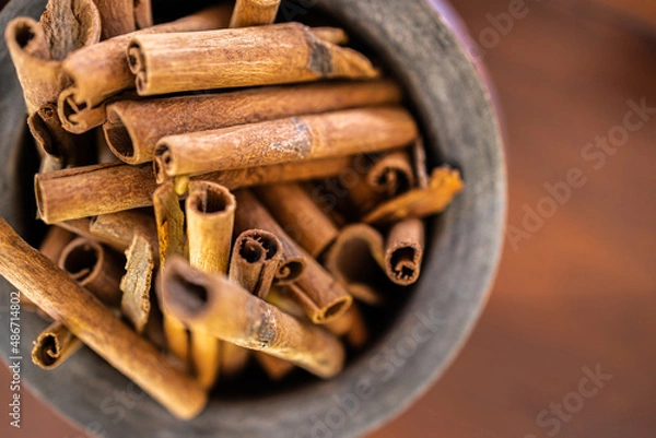 Fototapeta Wooden bowl top view with cinnamon sticks on dark wooden background. Abstract food and cooking ingredients for dessert and healthy meals