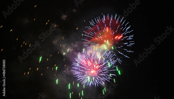 Fototapeta Colorful salute, great explodes in different colors in the night sky, beautifully dissolving in the air.
