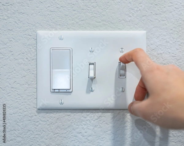 Fototapeta Closeup hand turning on-off switch after using, saving energy concept. Minimal design of mounted electricity control on the wall. Household electric outlet in home, residential, indoor room, apartment