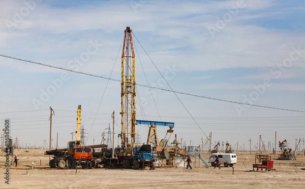 Fototapeta Works on oil drill rig. Workers, auto, trucks and pumping jack in desert. Zhanaozen, Kazakhstan.