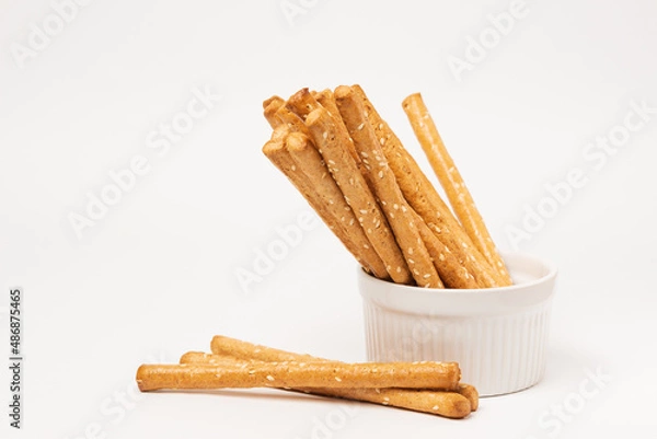 Fototapeta Classic crispy bread sticks grissini with sesame seeds in white form. Traditional Italian pastry breadsticks on white background with copy space